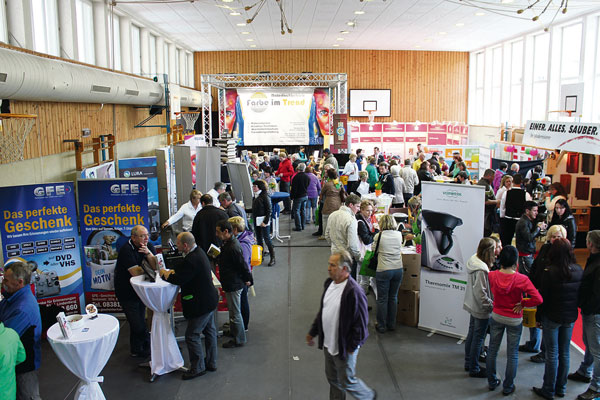 Die Sporthalle mit den verschiedenen Firmenständen, die auf der Ausstellung mit dabei sind. Es sind viele Besucher zu sehen.