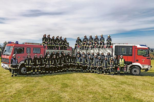 Mannschaft Feuerwehr Gestratz Zu sehen sind 2 Feuerwehrautos mit dem gesamten Feuerwehr-Team Gestratz in Feuerwehr-Uniform im Jubiläumsjahr.