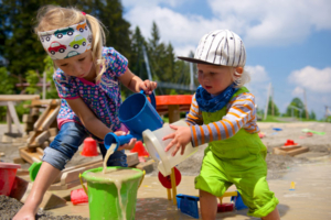 Wasserspielplatz Zwei kleine Kinder, ein Mädchen und ein Bub, spielen mit Eimern im Sand auf dem Wasserspielplatz.